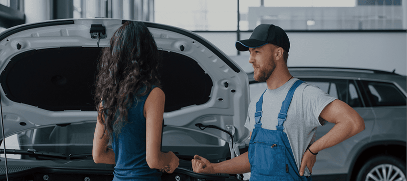 Technician talking with a customer beside a vehicle in the service bay