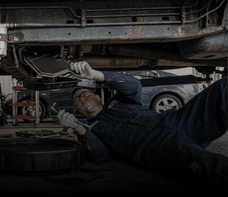 Mechanic working on transmission filter replacement under a vehicle
