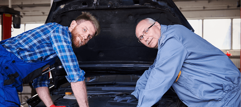 Two mechanics inspecting a car engine under the hood at Ten Minute Oil Change
