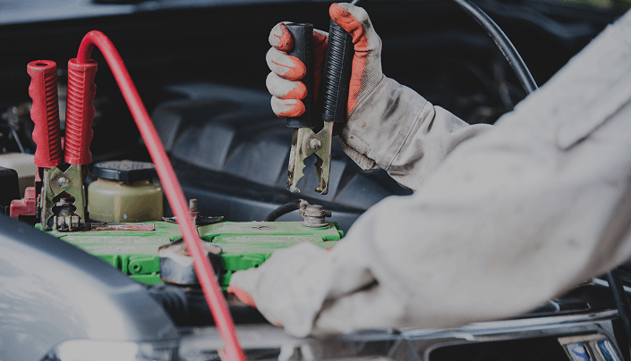 Technician testing a car battery with jumper cables in the engine bay