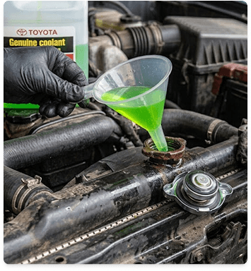 Gloved hands pouring green coolant into a vehicle reservoir