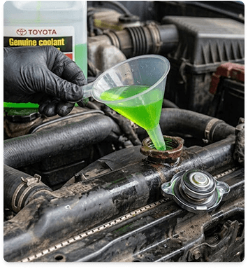Gloved hands pouring green coolant into a vehicle reservoir