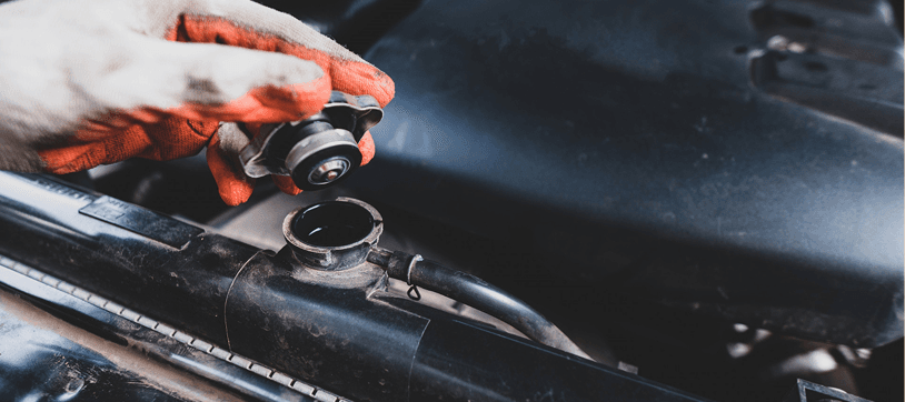 Gloved hand turning a metal radiator cap on a car radiator