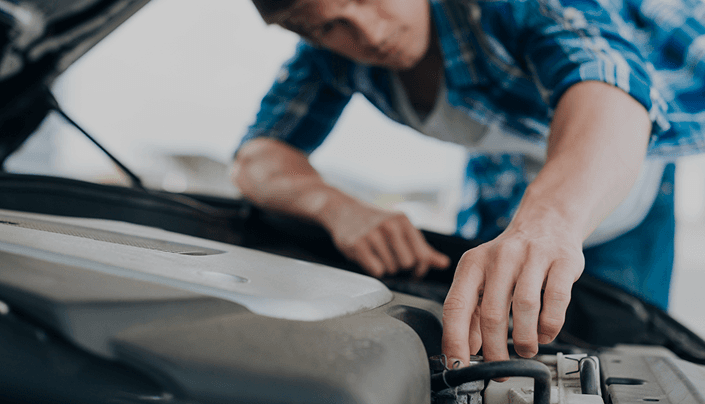 Technician in a blue plaid shirt working under an open car hood
