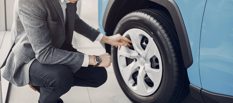 Technician checking tire pressure on a light blue car in a service bay