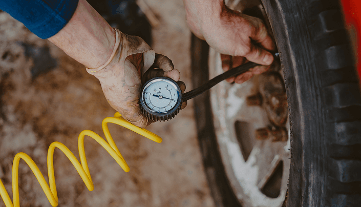 Hands checking tire air pressure with a gauge and yellow air hose