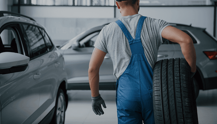 Technician carrying a tire through a service center with an SUV in the background