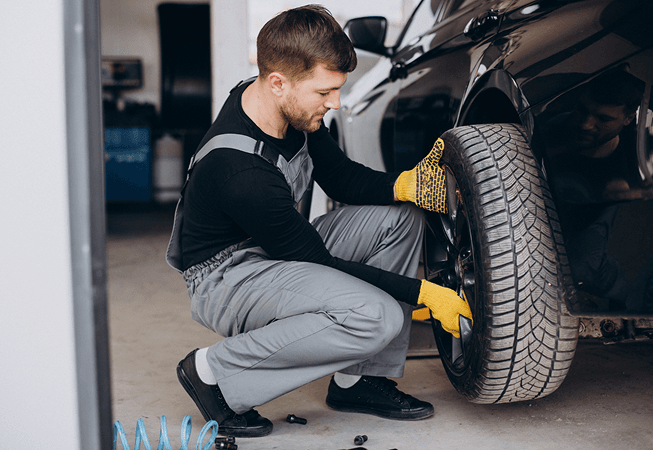 Technician installing a tire on a black car in a service bay