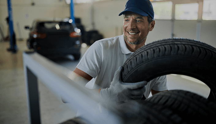Smiling technician in a blue cap working with a tire in the shop