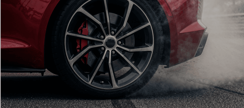 Close-up of a sports car wheel with red brake calipers and tire smoke