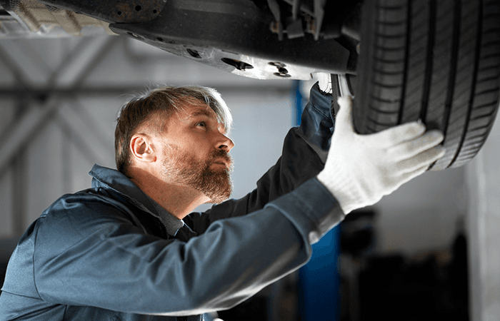 Technician inspecting a tire and brake area under a vehicle on a lift