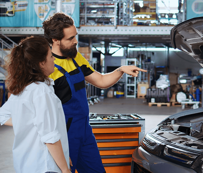 Technician explaining engine service to a customer under an open hood