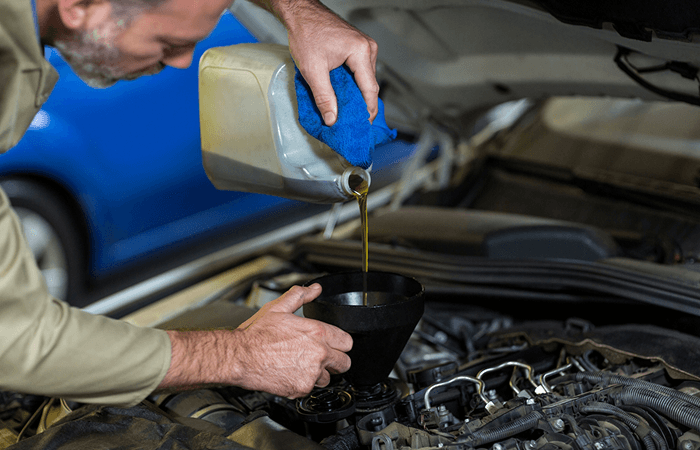 Mechanic pouring power steering fluid into a vehicle engine with a funnel