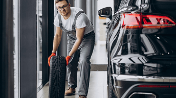Mechanic rolling a new tire next to a vehicle
