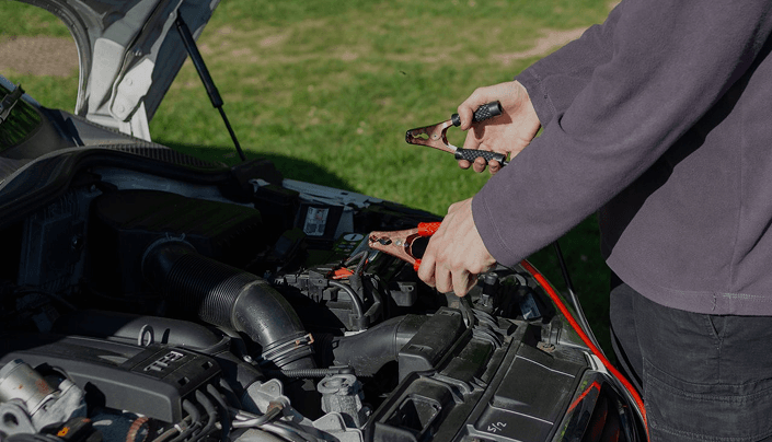 Technician connecting jumper cables to a car battery under the hood