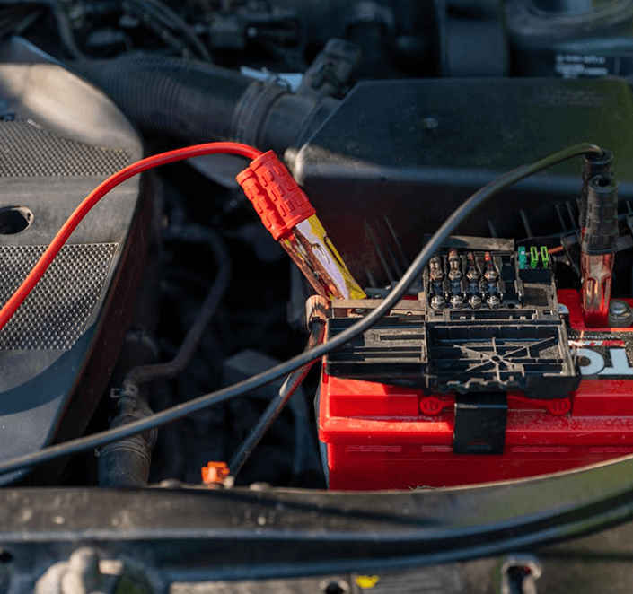 Car battery with jumper cable clamps attached in the engine bay