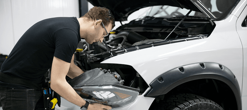 Mechanic repairing a car headlight in a Garland auto shop
