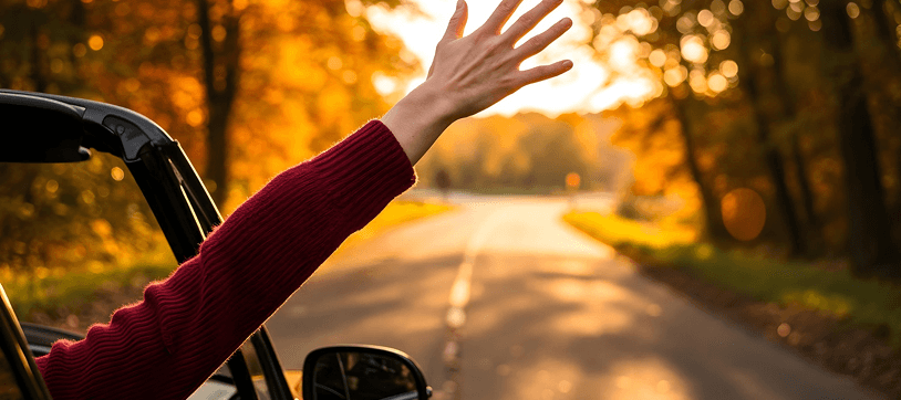 Hand reaching out of a car window on the road at sunset