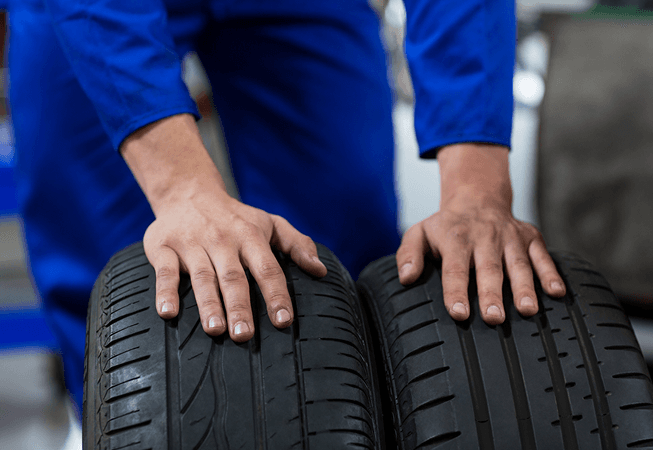 Technician in blue overalls resting hands on two upright car tires