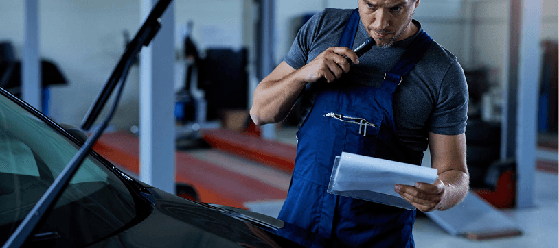 Mechanic with clipboard inspecting a vehicle in the auto shop